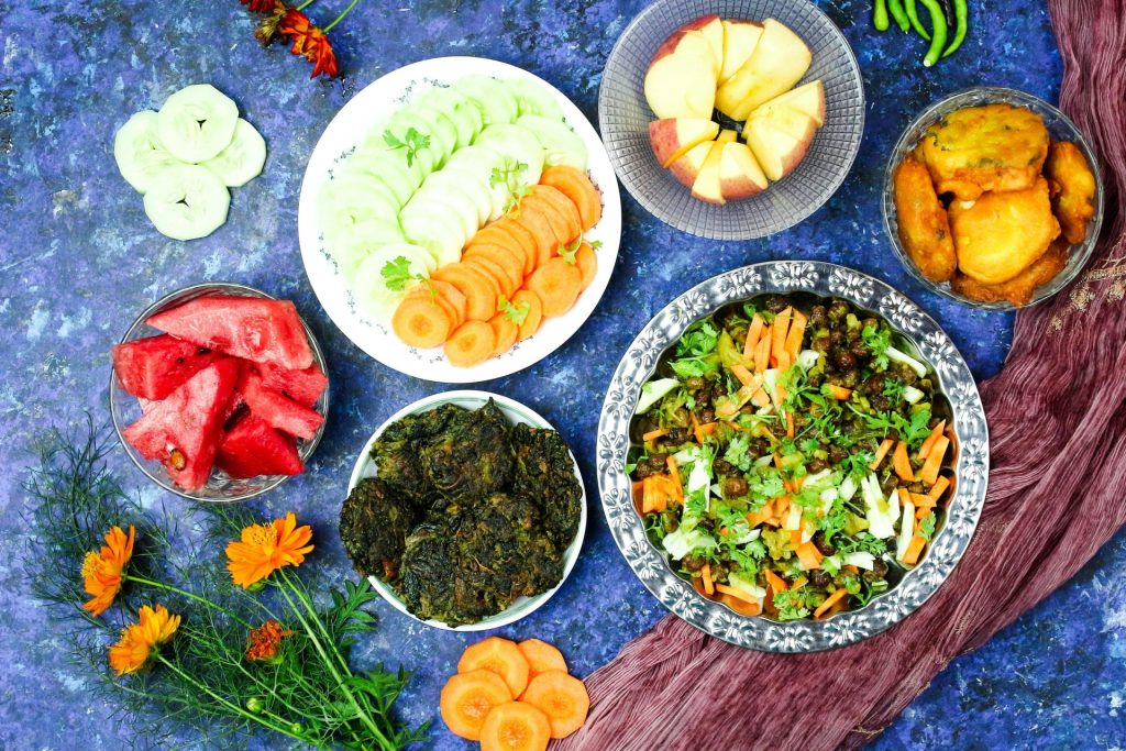 Eine lebendige Draufsicht auf ein farbenfrohes vegetarisches Menü mit Salaten und Früchten vor einem strukturierten Hintergrund.